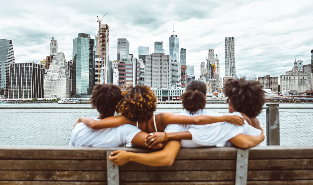 4 friends from being sitting on a bench in Brooklyn, New York, looking at Manhattan's skyline.