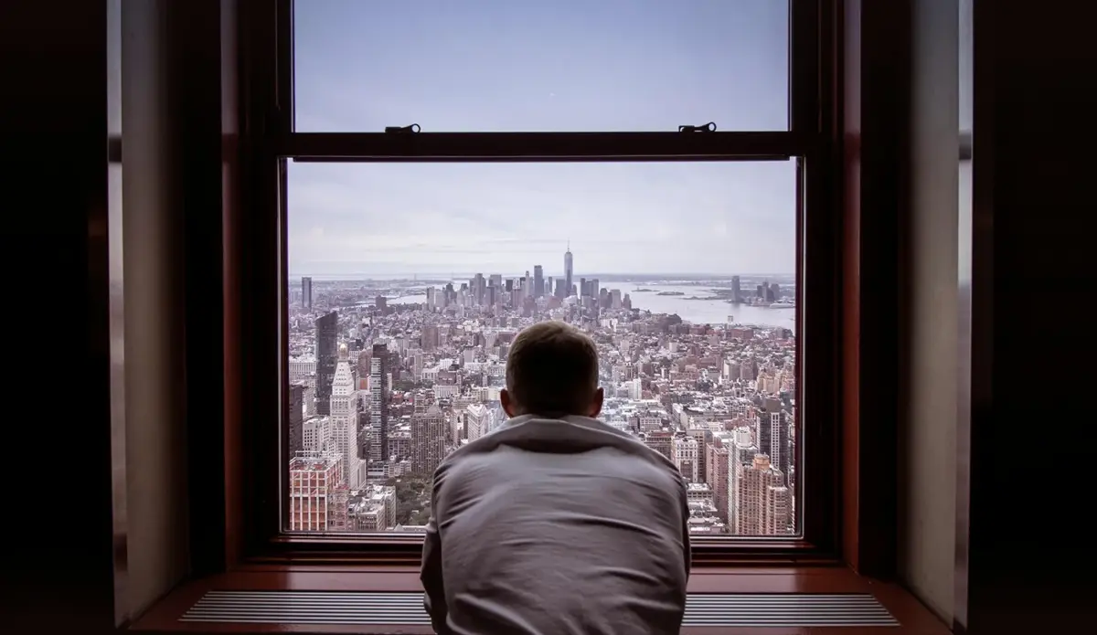 Man looking out of window from a Manhattan residential building - Moving to NYC